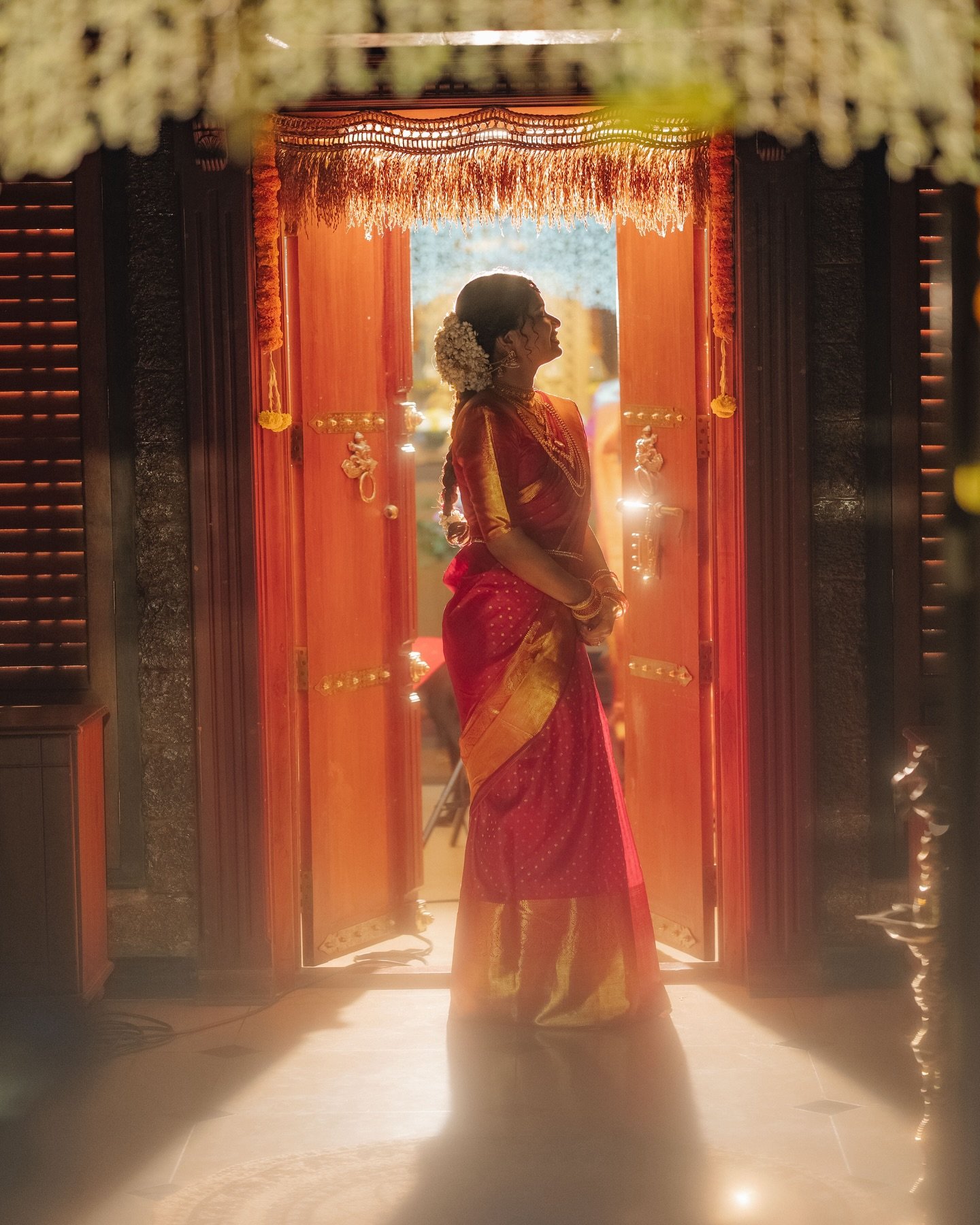 A bride in traditional crimson silk saree illuminated in temple doorway